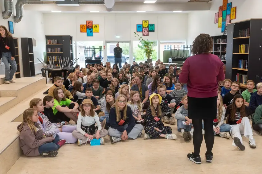 Skolebørn sidder på gulvet og lytter