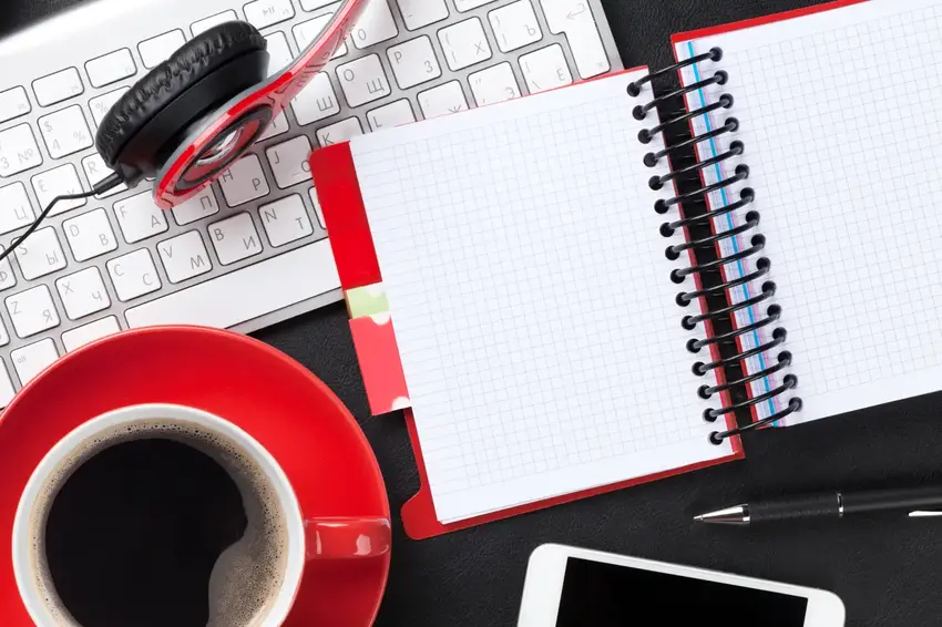 Pc keyboard med notesbog, rød kaffekop og hovedtelefoner