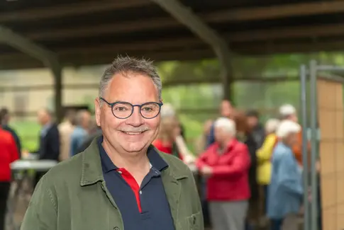 Mand med briller og jakke med mennesker i baggrunden