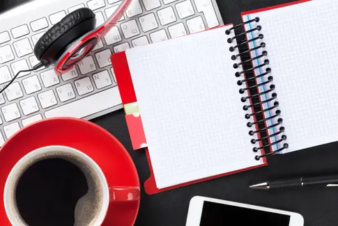 Pc keyboard med notesbog, rød kaffekop og hovedtelefoner