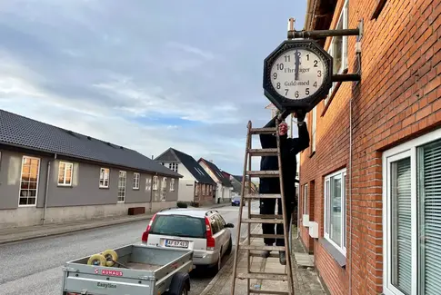 Mand på stige stiller et stort ur til klokken 12